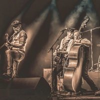 The Ridin' Dudes Vier Männer mit Gitarren, Kontrabassund Schlagzeug auf einer Bühne