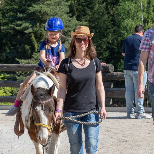 Kleines Mädchen sitzt auf Pony, das von einer Frau geführt wird