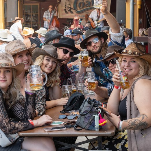 Menschen mit Cowboyhüten sitzen an einem Biertisch