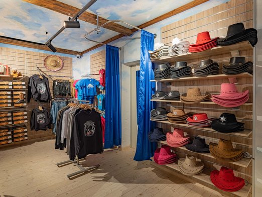 Pullover und T-shirts an Kleiderständer, Cowboyhüte in einem Regal