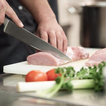 Professioneller Koch bei der Arbeit Koch schneidet Fleisch auf Brett