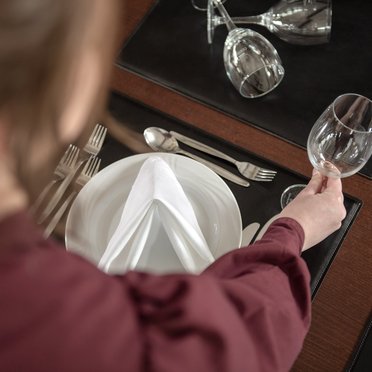 Fachkraft Restaurants & Veranstaltungsgastronomie Person platziert Geschirr auf einem Tisch