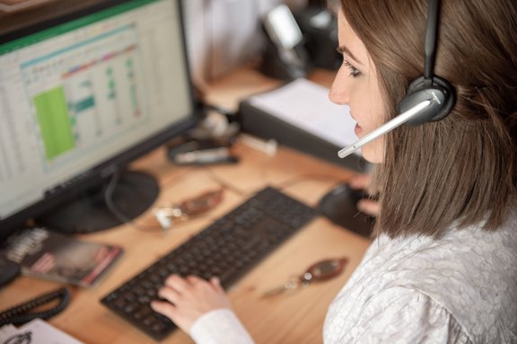Frau mit Headset sitzt an einem Schreibtisch mit PC