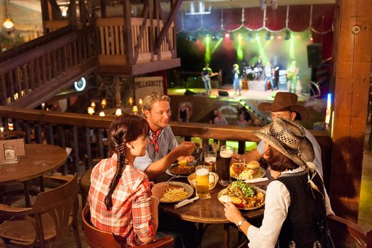 Die Musik and Dance Hall im Freizeitpark Pullman City Vier Personen sitzen um einen Tisch mit Essen
