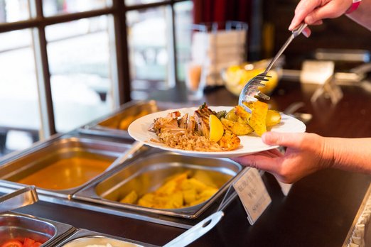 Eine Person legt sich Essen vom Buffet auf den Teller.