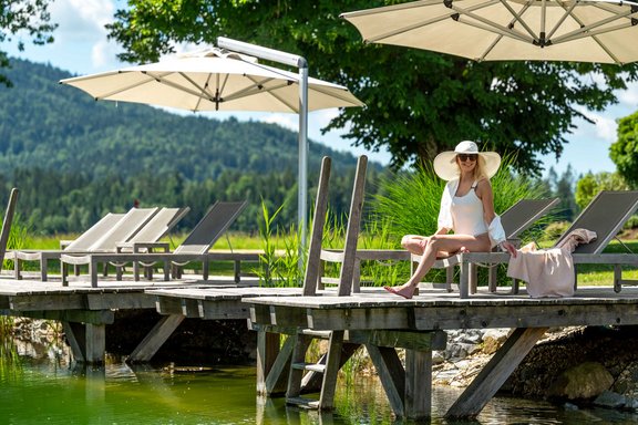 Frau sitzt auf einer Liege auf einem Steg in einen See
