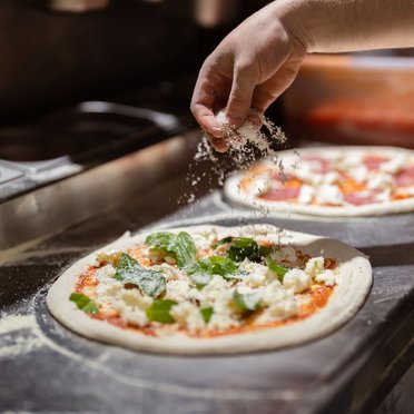 Frische Pizza in der Zubereitung Käse wird auf Pizza gestreut