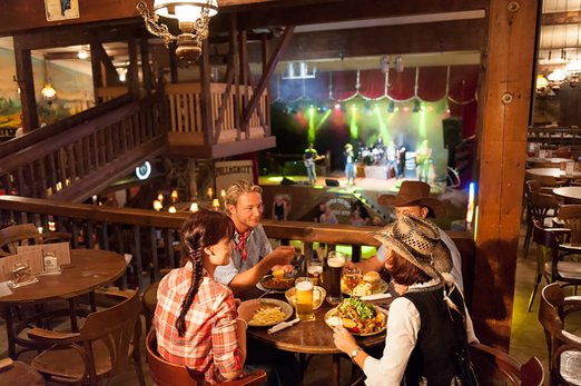 Vier Personen sitzen an einem Tisch mit Essen in der Music and Dance Hall der Westernstadt Pullman City