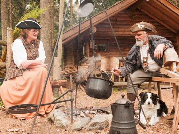 Mann und Frau mit Hund kochen über Lagerfeuer 